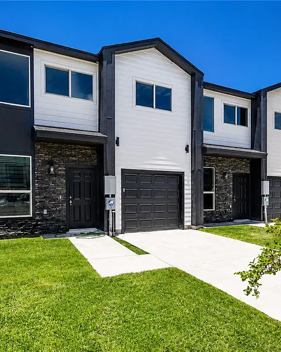 A row of two-story townhomes in white and black siding, with stone entries and single garages behind a new lawn